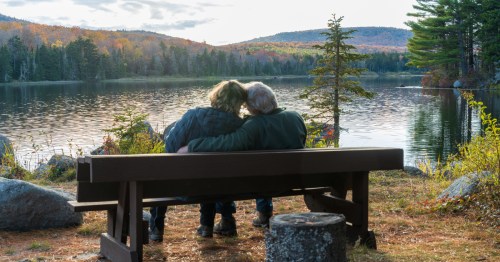 A couple sits on a bench near a lake in Vermont.
