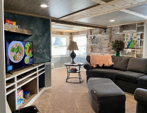 Cozy living room with a gray sectional, TV displaying food, lamp, and decorative wall art. Warm, inviting atmosphere.