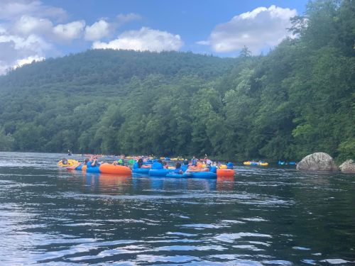 A group of people floating on colorful inner tubes in a river, surrounded by lush green trees and a blue sky.