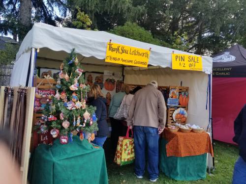 A festive market stall with a sign for a pin sale, decorated with a small tree and customers browsing.