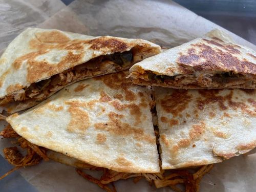 Three pieces of golden-brown quesadilla filled with shredded chicken and herbs, served on parchment paper.