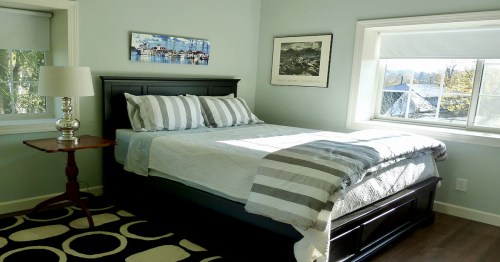 Cozy bedroom with a queen bed, striped bedding, a lamp, and a window letting in natural light.