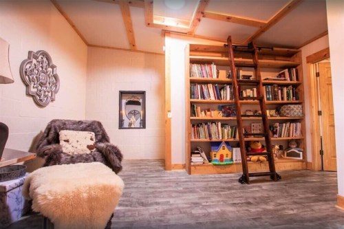 Cozy room with a bookshelf, ladder, armchair, and soft rug, featuring warm wood accents and a bright atmosphere.