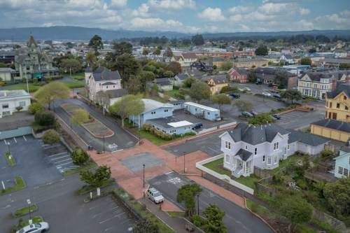 Aerial view of a small town with colorful houses, parking lots, and a cloudy sky in the background.