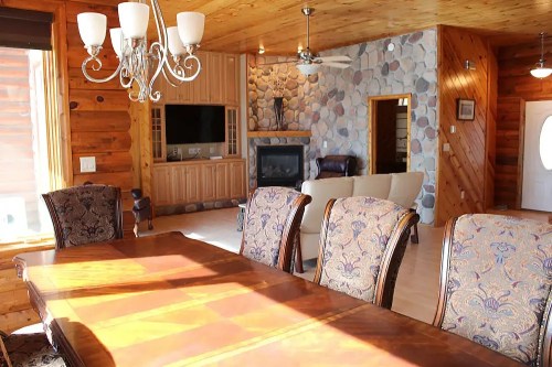 A cozy dining area with a wooden table, elegant chairs, and a stone fireplace in a rustic cabin setting.