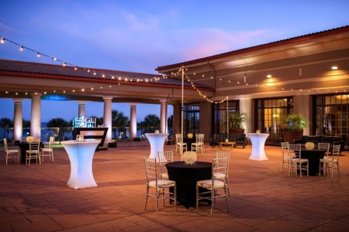 An outdoor event space with tables, chairs, and string lights, set against a twilight sky.