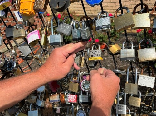 A person’s hands are attaching a padlock to a wall covered in various colorful locks.