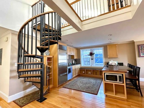 A modern kitchen with a spiral staircase, wooden floors, and a dining area featuring a microwave and bar stools.