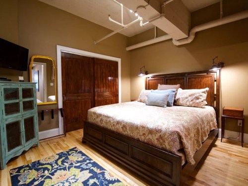 Cozy bedroom featuring a large bed, wooden furniture, a mirror, and warm-toned walls.