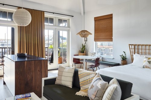 Bright, modern studio with a cozy seating area, dining table, and large windows showcasing a view. Warm, inviting decor.