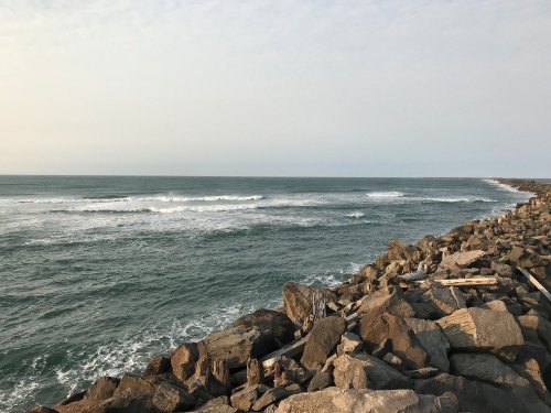A rocky shoreline with gentle waves lapping against the coast under a clear sky.
