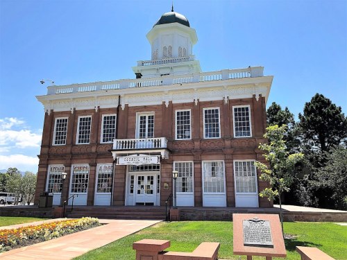 Historic building with a green dome, white trim, and large windows, surrounded by landscaped gardens and a plaque.