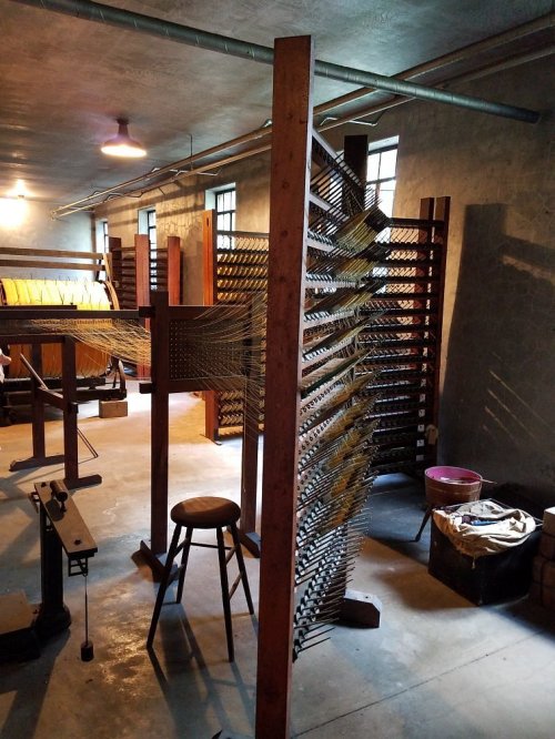 A workshop with wooden weaving equipment and tools, featuring a large loom and a stool in a well-lit space.
