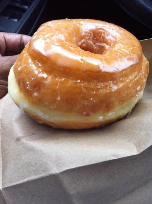 A glazed donut resting on a brown paper bag, showcasing its shiny, golden-brown surface.
