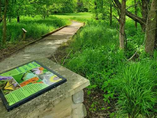 A pathway through lush greenery, with an informational sign about local flora and fauna in the foreground.