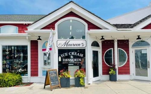 A charming ice cream shop with a red exterior, large windows, and a sign reading "Maureen's Ice Cream & Desserts."