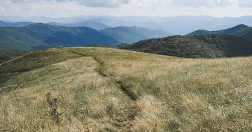 A trail winds through the grassy bald of Max Patch, NC, with mountains in the distance.