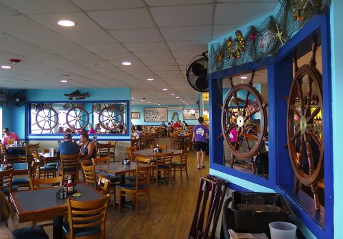 A vibrant restaurant interior featuring wooden ship wheels, blue walls, and diners enjoying their meals.