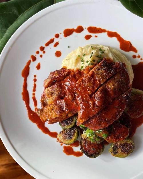 A plate featuring roasted chicken with sauce, Brussels sprouts, and creamy mashed potatoes, garnished with chives.