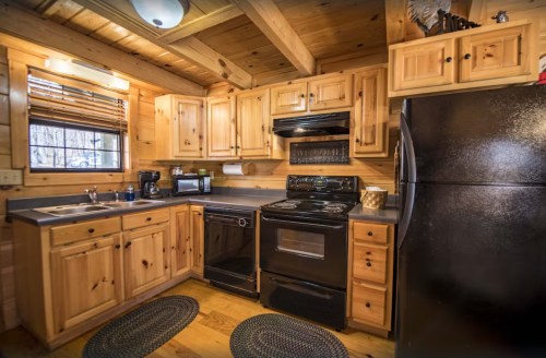 Cozy wooden kitchen with natural wood cabinets, black appliances, and a warm, rustic atmosphere.