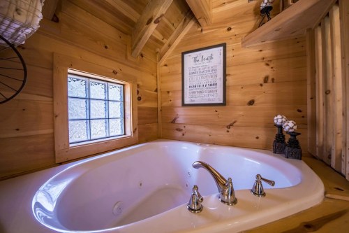Cozy wooden bathroom featuring a large white bathtub, a window, and decorative wall art.