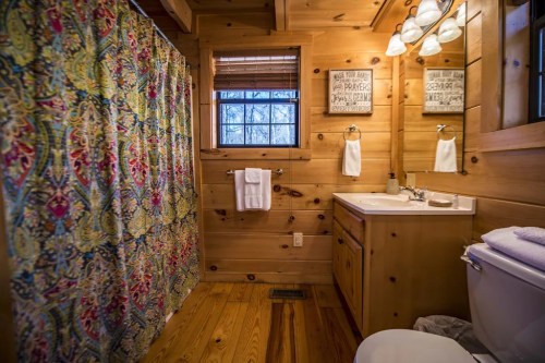 Cozy wooden bathroom featuring a colorful shower curtain, sink, and natural light from a window.