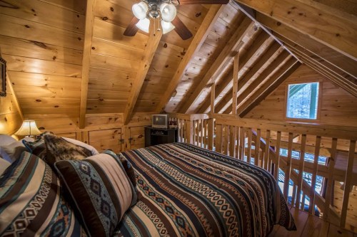 Cozy attic bedroom with wooden beams, a patterned bedspread, and a window letting in natural light.
