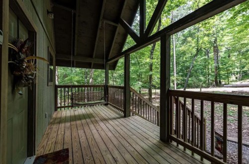 A wooden porch with a swing, surrounded by lush green trees and a peaceful forest setting.