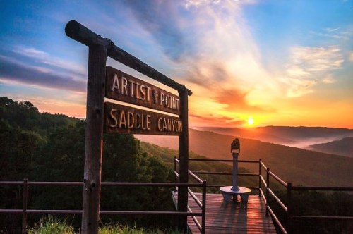 Sunrise over a valley viewed from Artist Point, with a sign for Saddle Canyon and a scenic overlook.
