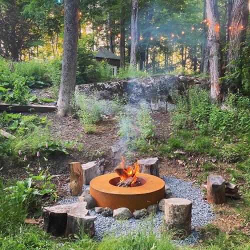 A cozy fire pit surrounded by logs and greenery, with smoke rising in a serene forest setting.