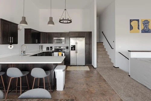 Modern kitchen with dark cabinets, stainless steel appliances, and a staircase leading to an upper level.
