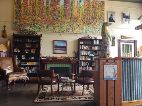 Cozy interior of a library with colorful artwork, bookshelves, and comfortable seating. A unique statue adds character.