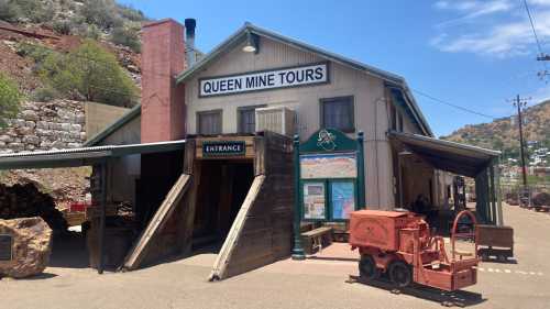 Historic building labeled "Queen Mine Tours" with an entrance and mining cart outside, set against a mountainous backdrop.