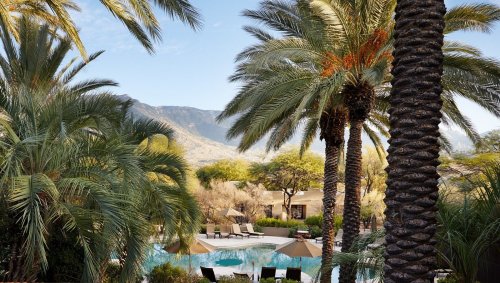 A serene pool surrounded by palm trees and mountains, creating a tranquil resort atmosphere.