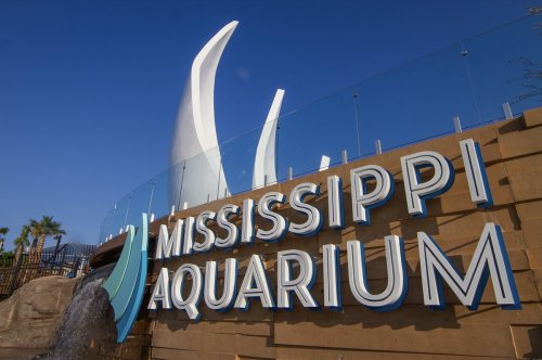 Sign for the Mississippi Aquarium with modern architecture and blue sky in the background.