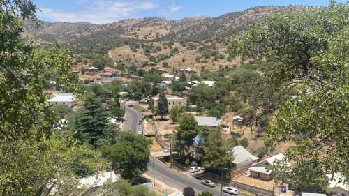 A scenic view of a hilly landscape with houses, trees, and a winding road under a clear blue sky.