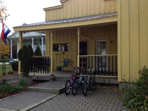 A yellow house with a porch, featuring two bicycles parked in front and a flag nearby.