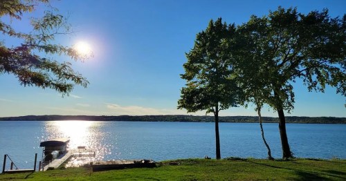 A serene lakeside view with sunlight reflecting on the water, framed by trees and a small dock.