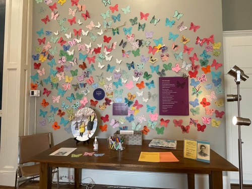 A wall covered in colorful paper butterflies, with a table displaying art supplies and informational materials.
