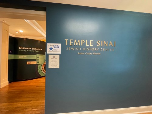 Entrance to Temple Sinai Jewish History Center, featuring a blue wall and informational displays about Judaism.