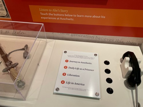 Display featuring a historical artifact, a phone, and an information sign about Abe's story and experiences in Auschwitz.