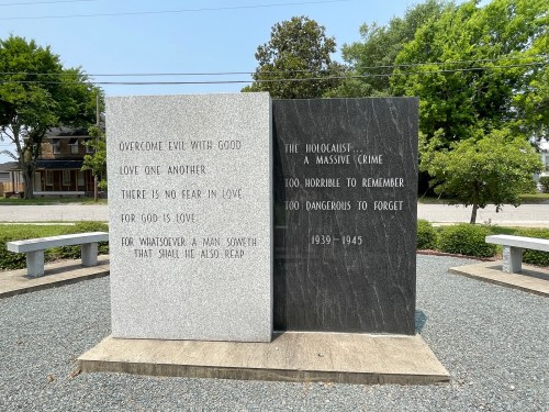 A memorial with two stone panels featuring inscriptions about love, evil, and the Holocaust, surrounded by greenery.