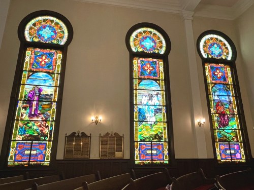 Three colorful stained glass windows depicting biblical scenes, illuminated in a church interior.