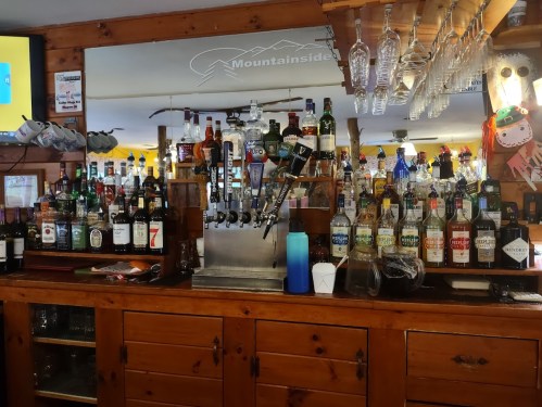 A wooden bar with various bottles of liquor and a beer tap, set in a cozy, rustic environment.