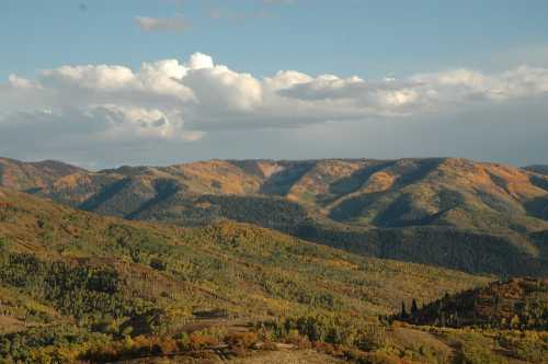 A scenic view of rolling mountains covered in autumn foliage under a partly cloudy sky.