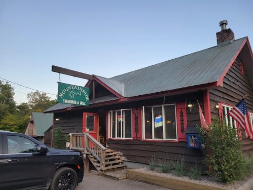 A rustic brown building with a green roof, sign reading "Mountain Side" and an American flag outside.