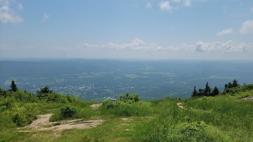 A panoramic view of a lush green valley under a clear blue sky with scattered clouds.