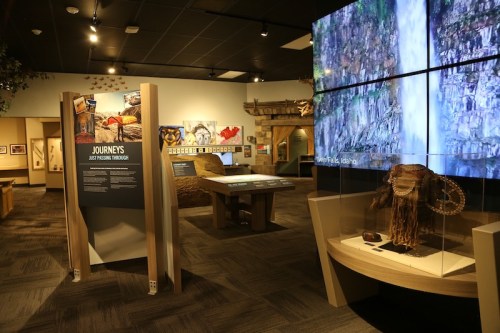 Exhibit space featuring informational displays, artifacts, and multimedia screens in a museum setting.