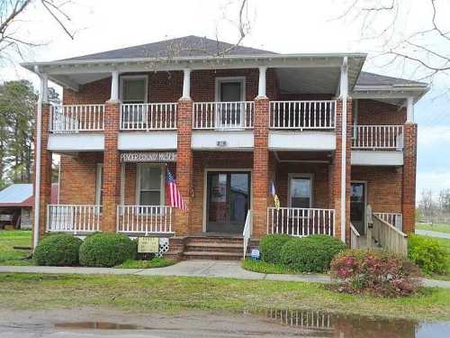 Two-story brick building with a porch, featuring American flags and a sign that reads "Pioneer County Museum."