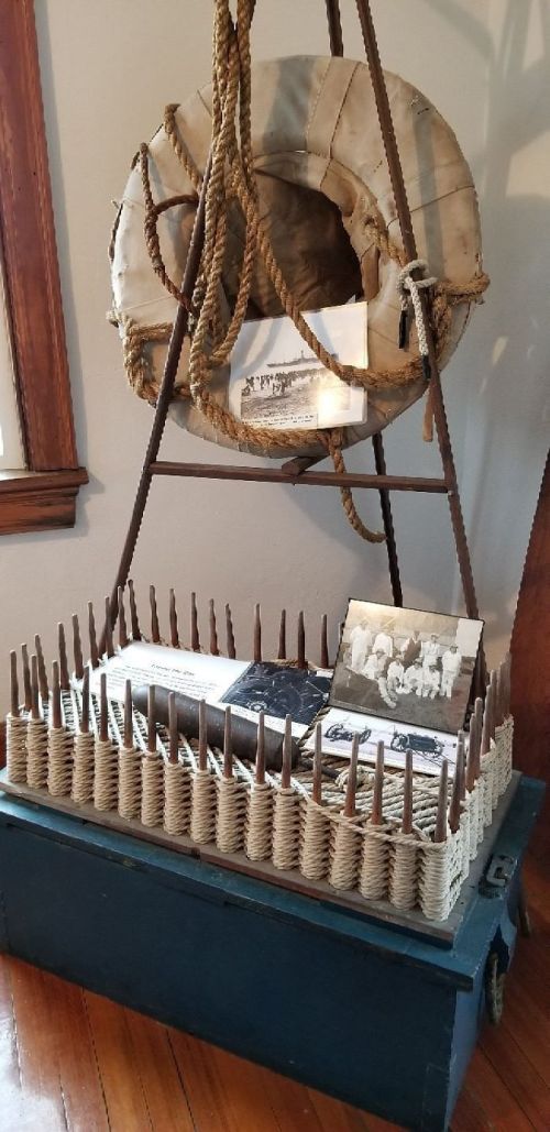 A vintage display featuring a life preserver, old photographs, and a wooden box with spikes arranged around it.